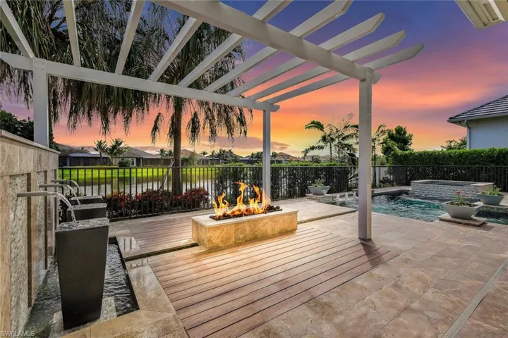 Patio terrace at dusk with a pergola, pool water feature, a pool with hot tub, and an outdoor fire pit