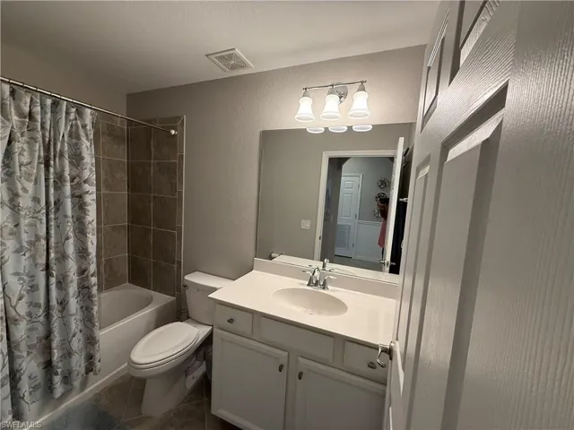 Bathroom featuring a textured wall, shower / tub combo, vanity, and dark tile patterned flooring