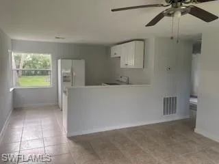 Kitchen featuring white cabinets, range, a ceiling fan, white fridge with ice dispenser, and a peninsula