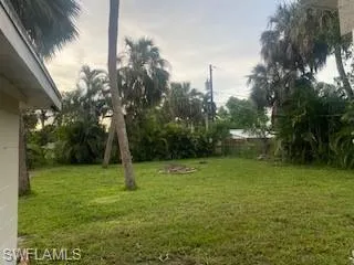 View of back yard with green lawn and wooded view.
