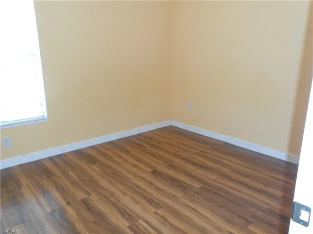 Unfurnished room featuring dark wood-style flooring and baseboards