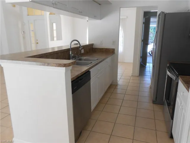Kitchen with stainless steel appliances, white cabinets, light tile patterned flooring, dark countertops, and a peninsula
