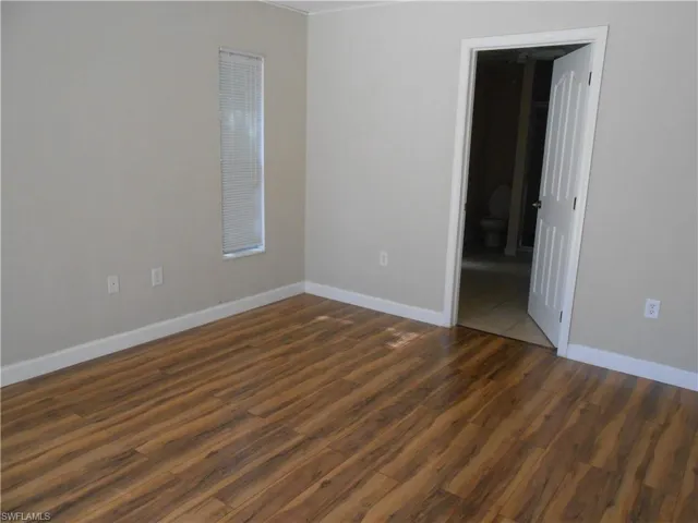 Unfurnished room with baseboards and dark wood-type flooring