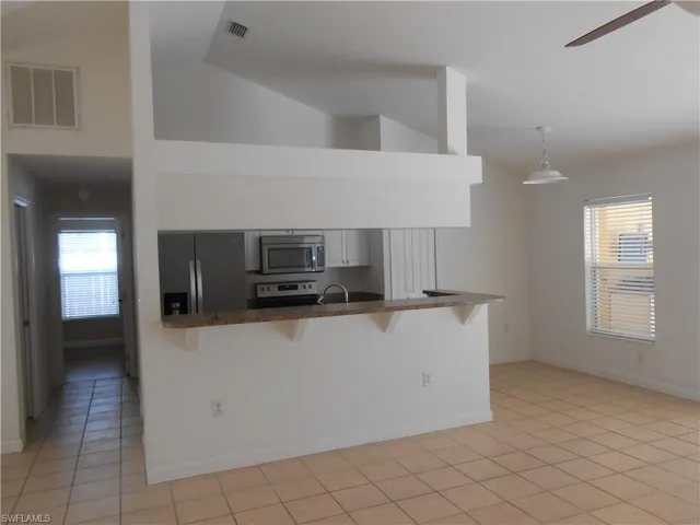 Kitchen featuring a breakfast bar, stainless steel appliances, vaulted ceiling, ceiling fan, and hanging light fixtures