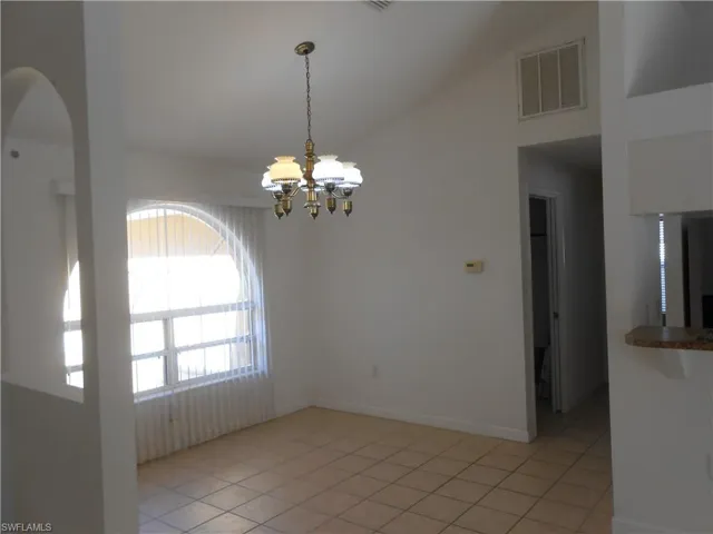 Empty room with a chandelier, vaulted ceiling, and light tile patterned floors