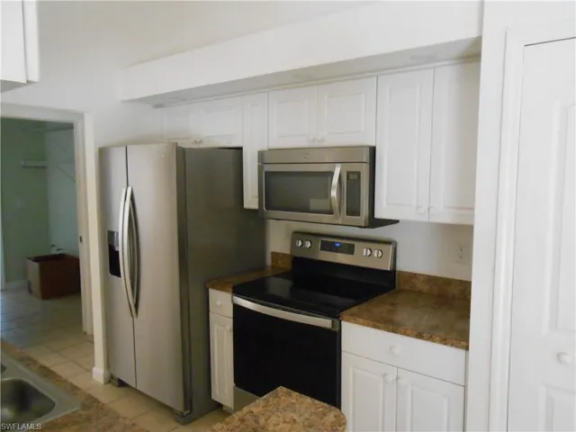 Kitchen featuring stainless steel appliances, white cabinets, light tile patterned floors, and dark countertops