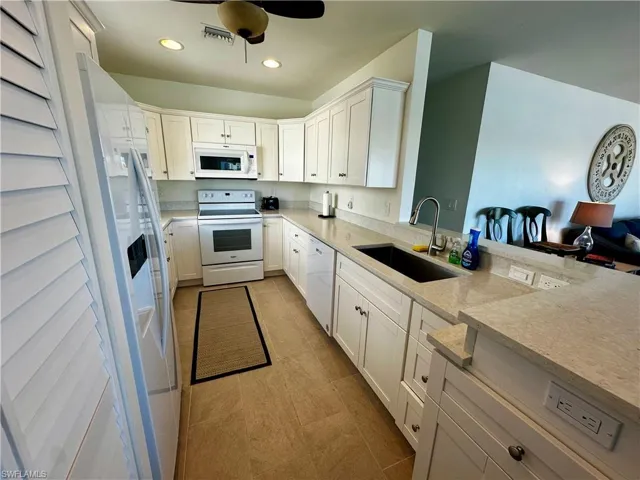 Kitchen with white cabinetry, white appliances, light stone counters, recessed lighting, and a ceiling fan