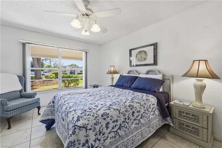 Bedroom with a textured ceiling, a ceiling fan, and light marble finish floors