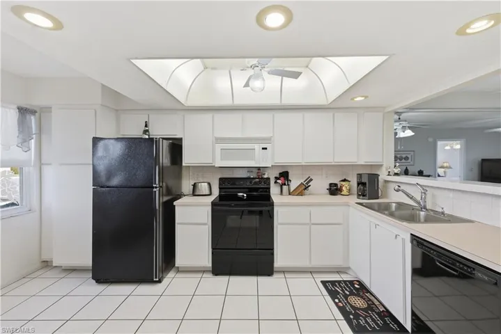 Kitchen with black appliances, light countertops, white cabinetry, recessed lighting, and decorative backsplash