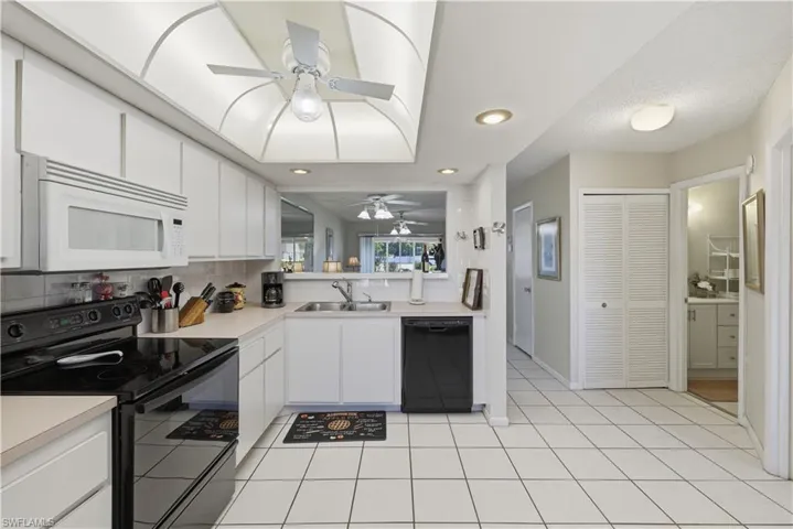 Kitchen with black appliances, light countertops, white cabinets, ceiling fan, and decorative backsplash