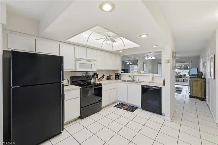 Kitchen with black appliances, light countertops, white cabinetry, recessed lighting, and decorative backsplash
