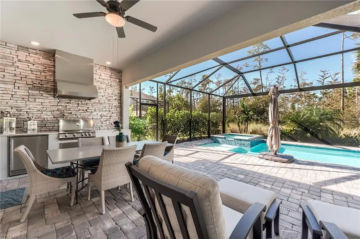 View of patio with an outdoor kitchen, glass enclosure, a pool with hot tub, and a grill