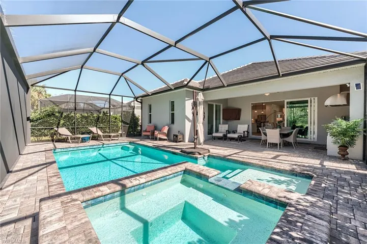View of pool with glass enclosure, a patio area, an outdoor hangout area, and an in ground hot tub