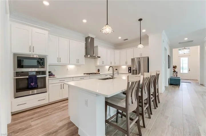 Kitchen featuring wall chimney exhaust hood, stainless steel appliances, a kitchen island with sink, sink, and pendant lighting