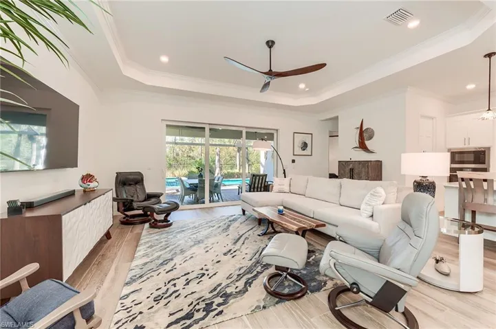 Living room with light wood-type flooring, a raised ceiling, ceiling fan, and ornamental molding