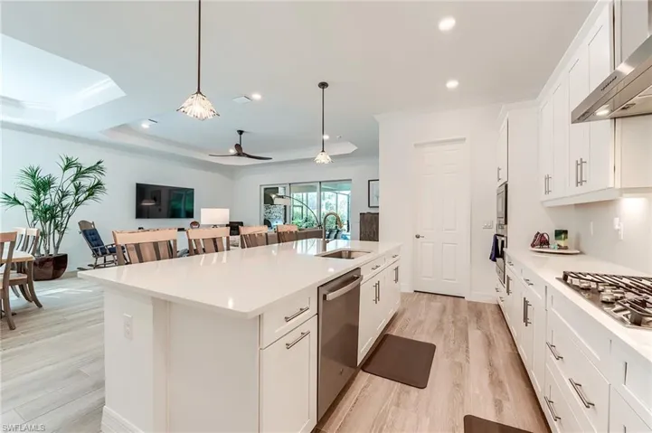 Kitchen with appliances with stainless steel finishes, a center island with sink, white cabinetry, and wall chimney range hood