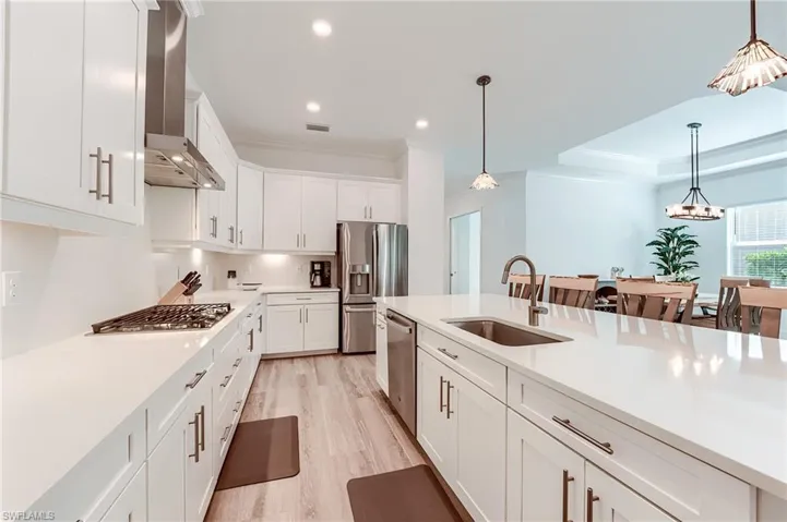 Kitchen with white cabinets, decorative light fixtures, wall chimney range hood, and sink