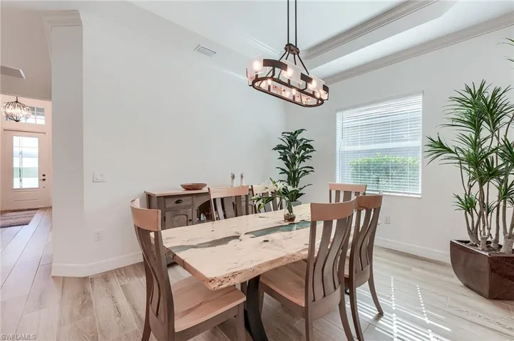 Dining space featuring light hardwood / wood-style floors, a raised ceiling, crown molding, and an inviting chandelier