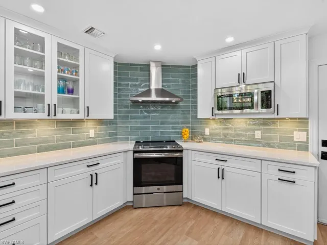 Kitchen with appliances with stainless steel finishes, wall chimney range hood, white cabinets, light wood-style floors, and recessed lighting