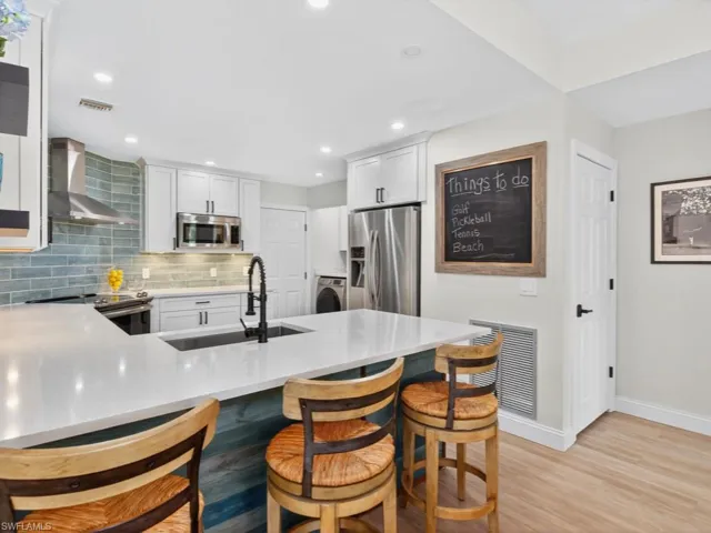 Kitchen with a peninsula, tasteful backsplash, a kitchen bar, wall chimney exhaust hood, and light stone countertops