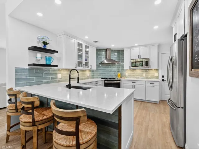 Kitchen with light stone counters, open shelves, a peninsula, a breakfast bar area, and white cabinets