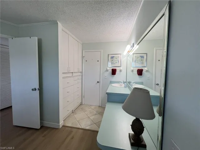 Full bathroom featuring light wood-type flooring, vanity, a textured ceiling, and crown molding