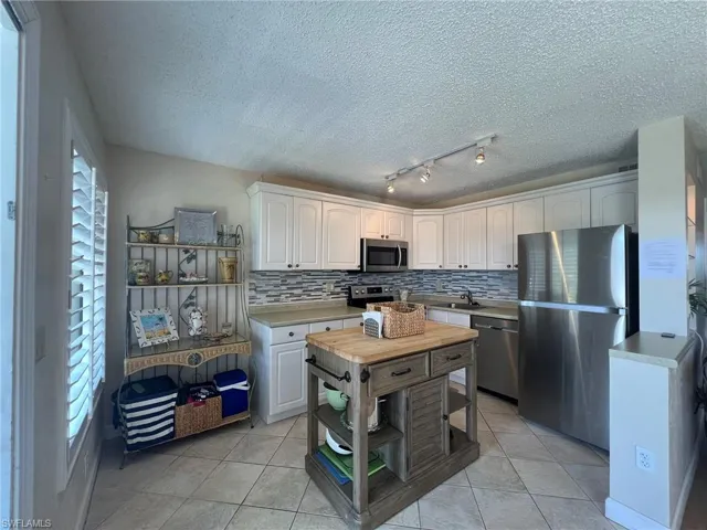 Kitchen featuring stainless steel appliances, light tile patterned flooring, light countertops, decorative backsplash, and a textured ceiling