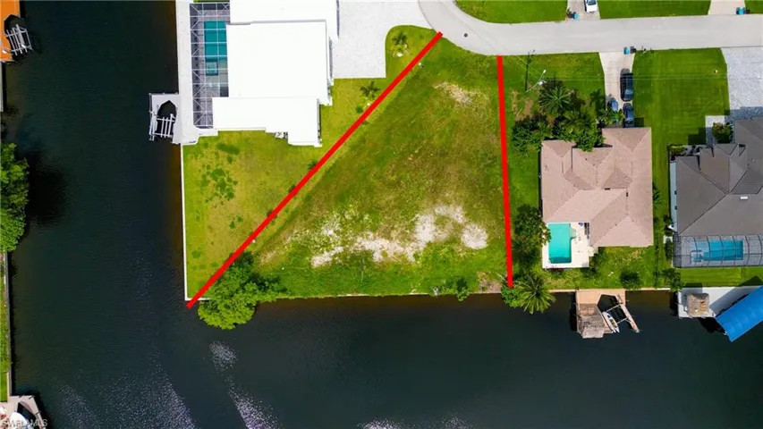 Expansive waterfront lot featuring direct canal frontage, a verdant grass expanse, and established tropical foliage
