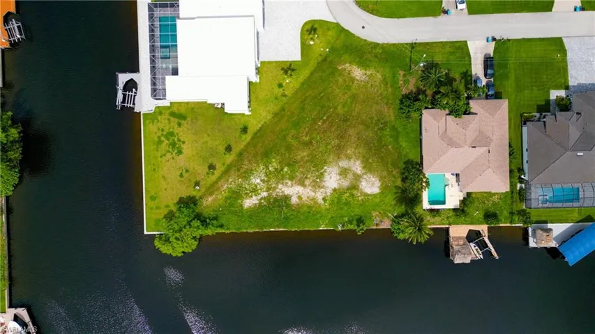 Waterfront lot featuring a wide canal, adjacent new construction, street access, and a clear building envelope