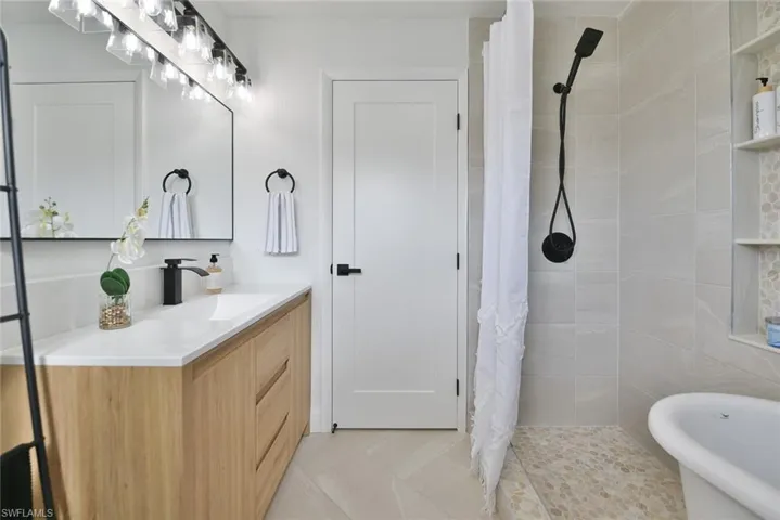 Full bath with vanity, a shower stall, a freestanding tub, and light tile patterned flooring