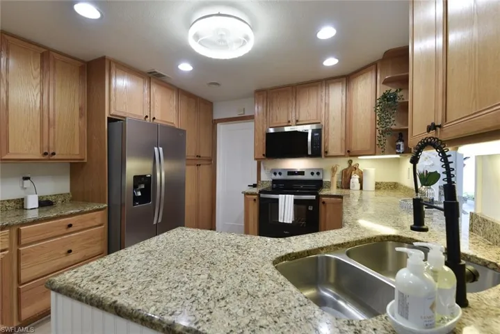 Kitchen with open shelves, light stone countertops, stainless steel appliances, and recessed lighting
