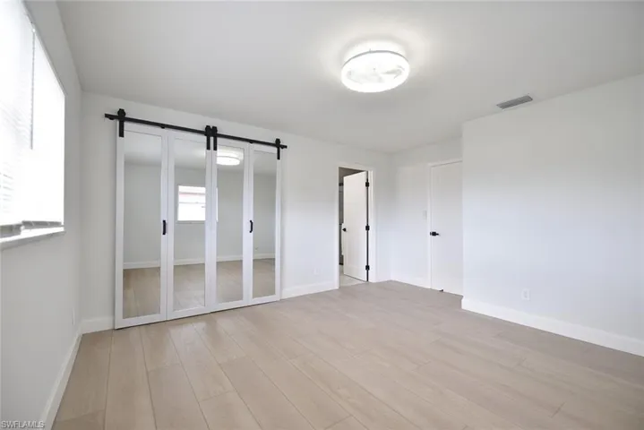 Unfurnished bedroom featuring light wood-type flooring, a barn door, and a closet