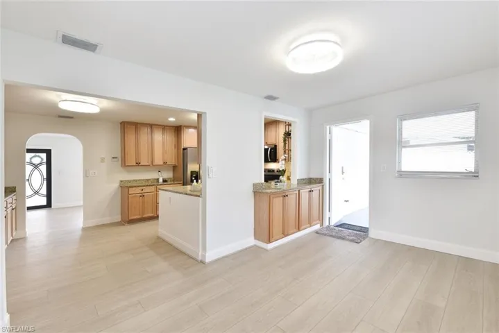Kitchen with arched walkways, light stone counters, light wood finished floors, and stainless steel appliances
