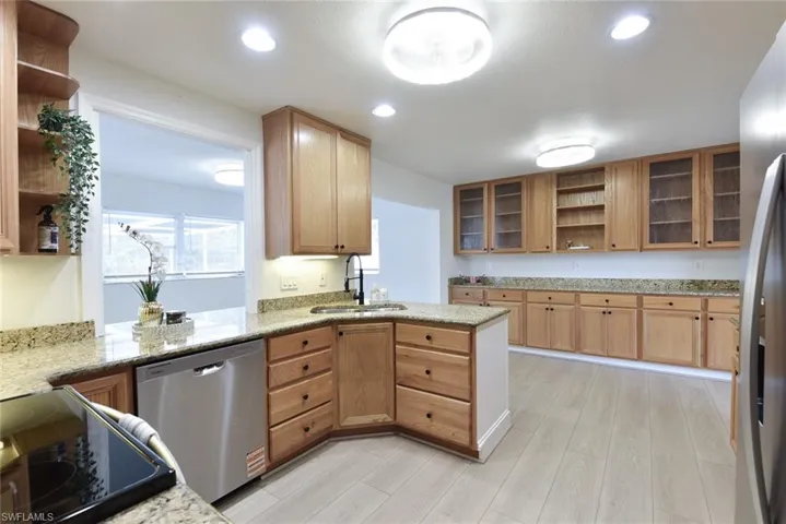 Kitchen featuring open shelves, glass fronted cabinets, stainless steel appliances, light stone counters, and recessed lighting