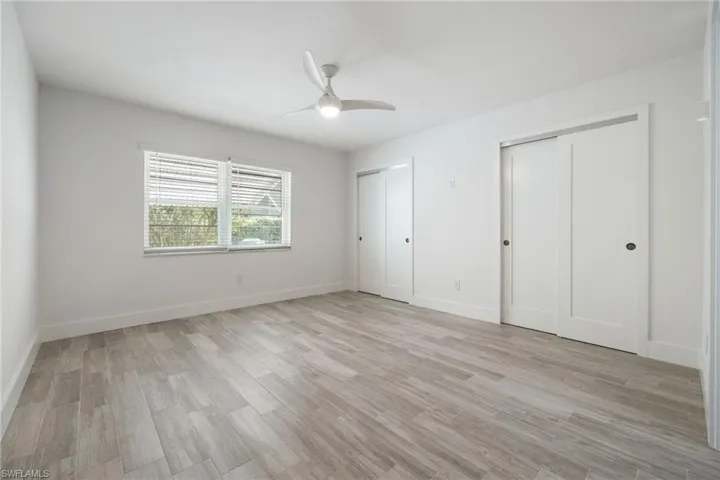 Master bedroom with two closets, light wood finished floors, baseboards, and ceiling fan.