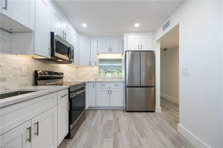 Kitchen with stainless steel appliances, white cabinetry, decorative backsplash, baseboards, and light countertops