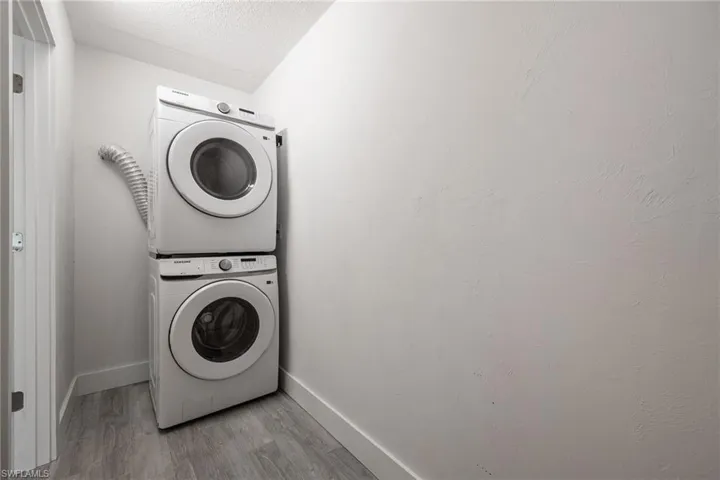 Laundry area with new stacked front-load washer / dryer, wood finished floors, baseboards, and a textured ceiling