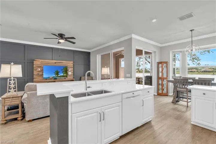 Kitchen featuring dishwasher, hanging light fixtures, white cabinets, sink, and a center island with sink
