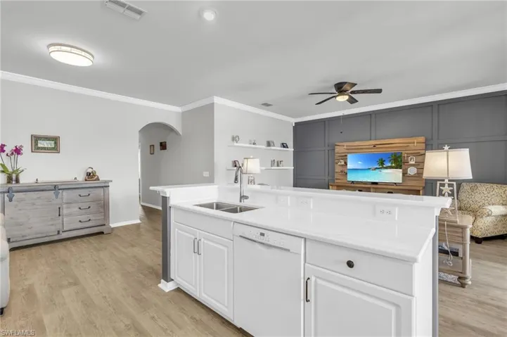 Kitchen with dishwasher, white cabinetry, an island with sink, sink, and crown molding