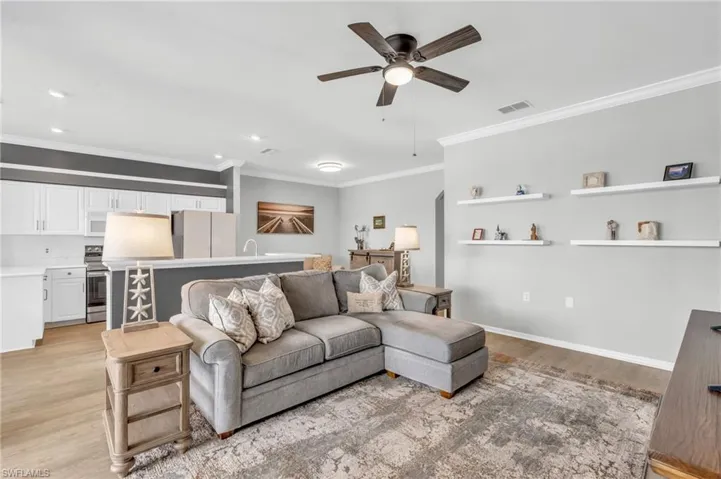 Living room with light hardwood / wood-style floors, ornamental molding, and ceiling fan