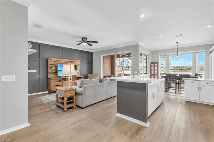 Kitchen featuring crown molding, light hardwood / wood-style floors, white cabinetry, decorative light fixtures, and a center island with sink