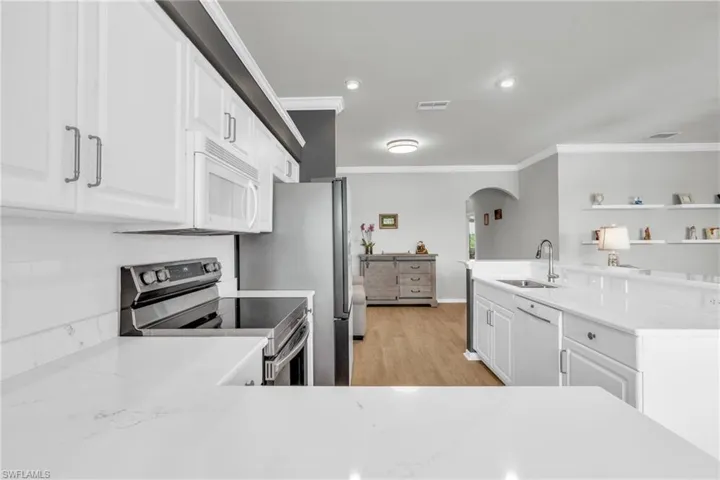 Kitchen featuring white appliances, white cabinets, sink, ornamental molding, and light stone counters
