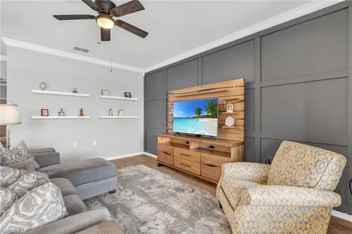 Living room with ceiling fan, dark wood-type flooring, and ornamental molding