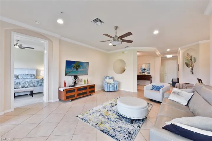 Living room with light tile patterned flooring, crown molding, and ceiling fan