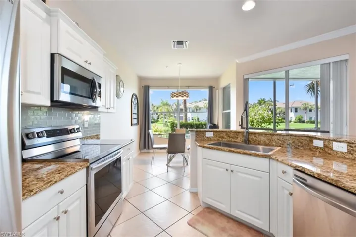 Kitchen with stainless steel appliances, sink, backsplash, decorative light fixtures, and light tile patterned flooring