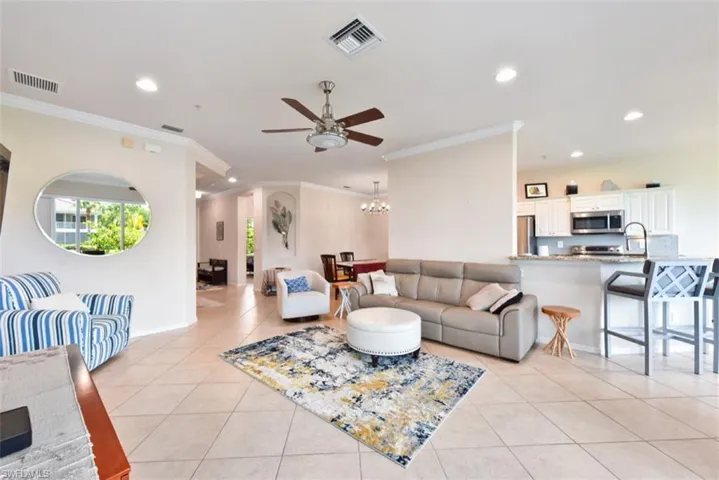 Living room with ceiling fan with notable chandelier, crown molding, sink, and light tile patterned floors