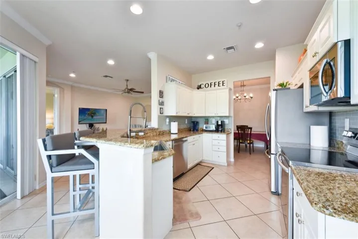 Kitchen with ceiling fan with notable chandelier, kitchen peninsula, backsplash, and stainless steel appliances