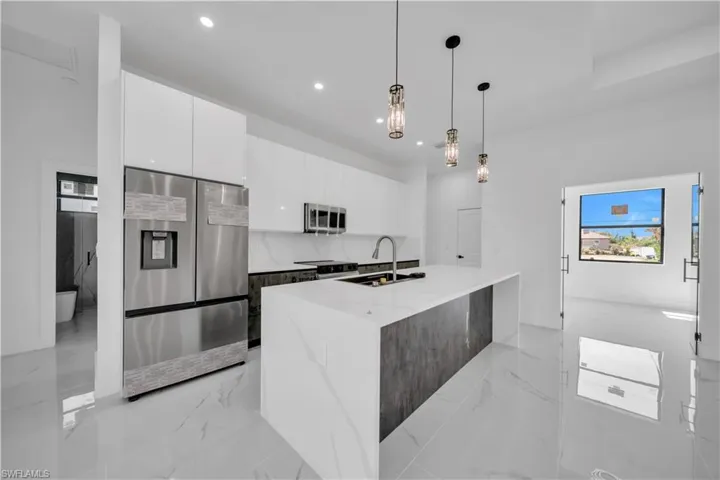 Kitchen featuring stainless steel appliances, modern cabinets, light stone counters, two tone cabinets, and hanging light fixtures