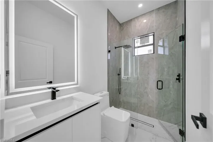 Bathroom featuring vanity, a marble finish shower, recessed lighting, and light marble finish floors
