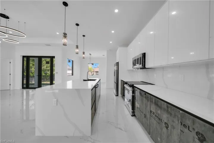 Two tone kitchen featuring stainless steel appliances, a large island, two tone color scheme, light stone counters, and pendant lighting
